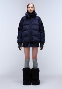 Námořnická zateplená péřová bunda s vysokým límcem, vroubkovaná textura, šedé vroubkované návleky na nohy a černé chlupaté boty do kotníků. Úzký střih.