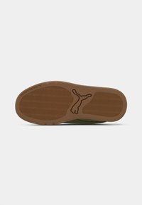 Brūnā gumijas zole treniņbiksēm ar viļņveida zīmējumu un Puma logo centrā, kas izskatās kā lecoša kaķis.