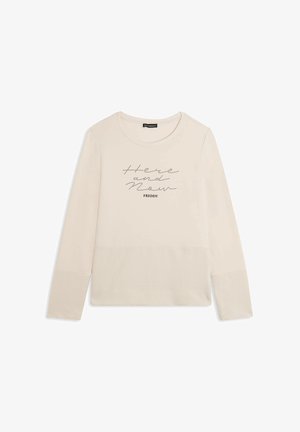 Top color crema chiaro a maniche lunghe in tessuto morbido con scollo rotondo. Presenta dettagli testurizzati sulle maniche e scritte stampate, "Qui e Ora."