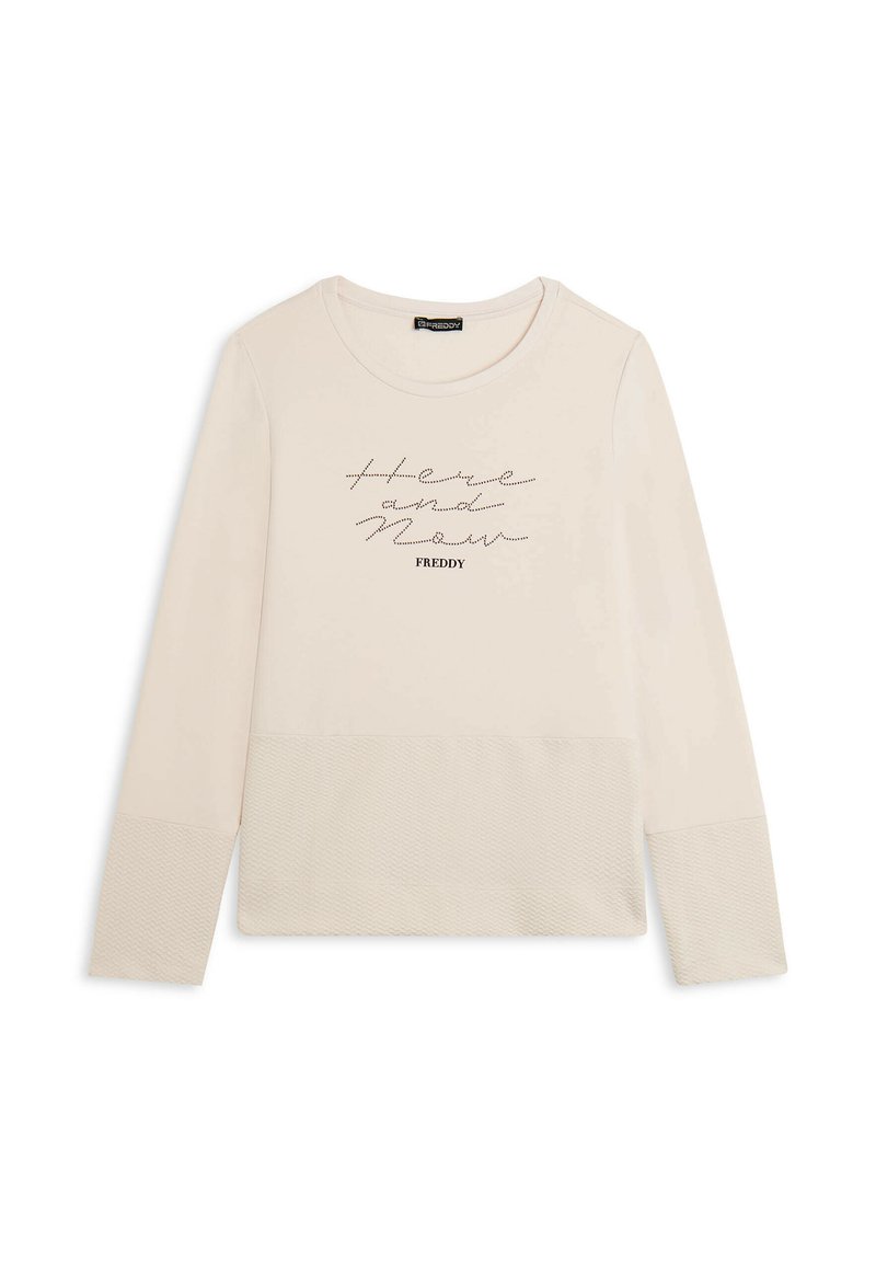 Top de manga larga color beige claro hecho de tela suave con un escote redondo. Presenta detalles texturizados en las mangas y letras impresas que dicen "Aquí y Ahora."