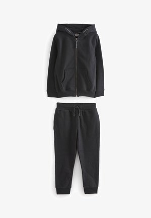 Melna jaka ar vizu no rāvējslēdzēja, divām priekšējām kabatām un oderētu kapuci, apvienota ar atbilstošām sporta biksēm, kuru viduklis ir elastīgs un ar saites pietvērēju.