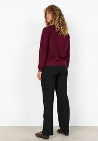 Maglione in lana borgogna con maniche lunghe, abbinato a pantaloni neri a costine, caratterizzati da una vestibilità rilassata e una trama sottile. Scarpe basse marroni con decorazioni.