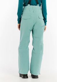 Jasnoniebieskie spodnie narciarskie z szelkami, o gładkiej fakturze, z bocznymi kieszeniami i rozszerzającymi się nogawkami, zaprojektowane do aktywności w zimnych warunkach.