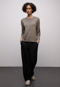 Pull en maille brun clair avec col rond, manches longues et poignets côtelés, associé à un pantalon noir ample et des baskets beiges.