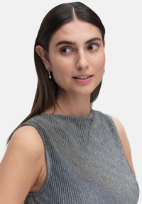 Ärmlös, ribbad topp i metallisk grå med rund halsringning. Modellen bär enkla silverörhängen med en slät, böjd design.