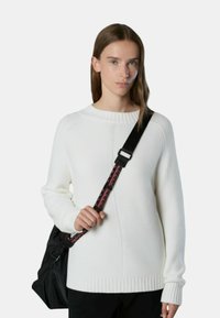 Maglione bianco lavorato a maglia con scollatura e polsini a coste; motivo testurizzato. Indossato con una borsa nera con tracolla decorativa.