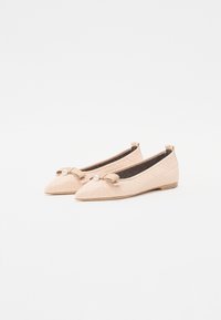 Ballerines matelassées nues avec un bout pointu, ornées d'un accent en nœud et d'un détail en perle, reposant sur un petit talon en bois.