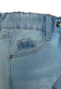 Svetle modré denimové šortky s elastickým pasem, malou přední kapsou a kontrastním hnědým prošitím.