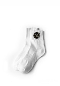 Calcetines tobilleros de algodón blanco con puño acanalado, con un parche redondo de logo negro en un lado. Textura suave y diseño simple.