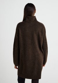 Vestito a maglia marrone con collo alto, maniche ampie e finitura tessurizzata. Progettato per una vestibilità morbida, arrivando a metà coscia.