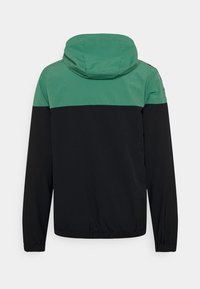 Huvjacka med en grön övre del och en svart underdel. Har elastiska ärmslut och dragsko i nederkant. Tillverkad av lätt material.