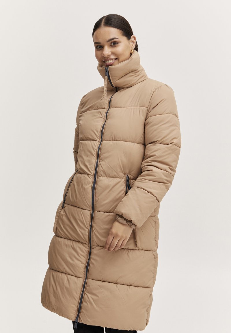 Beige pufferjacka med hög krage, dragkedjestängning och sidofickor. Har quiltade sektioner och elastiska ärmslut för en tight passform.