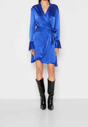 Satin wrap dress in royal blue, featuring long sleeves with flared cuffs, a side tie detail, and a knee-length hem. Paired with black knee-high boots.