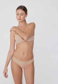 Beige Unterwäsche bestehend aus einem leicht gepolsterten BH mit dünnen Trägern und passendem nahtlosen Bikini-Höschen, beide aus einem weichen, glatten Material.