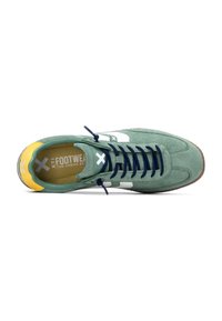 Zapatillas de gamuza verde con acentos en blanco y azul marino, talón amarillo y cordones azul marino. Presentan una superficie texturizada y suela de goma.