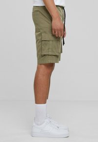 Khaki cargo shorts with multiple side pockets, drawstring waist, and a relaxed fit, worn with white sneakers and ankle socks.