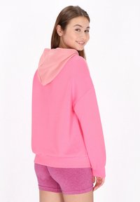 Hoodie rosa con motivi geometrici testurizzati e cappuccio a contrasto, abbinato a pantaloni corti rosa coordinati. Tessuto morbido, vestibilità ampia e maniche lunghe.