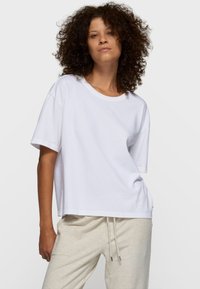 Hvid bomulds-T-shirt med rund halsudskæring, sænket skulder og afslappet pasform. Har diskret logodetalje på brystet.