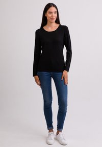 Schwarzes Langarmoberteil mit rundem Ausschnitt, kombiniert mit blauen Skinny-Jeans und weißen Sneakers. Glatte Textur und taillierte Passform.