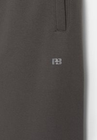 Grå mjukisbyxor i ett mjukt tyg har en diskret logotyp, fickor och en avslappnad passform som betonar komfort och funktionalitet.