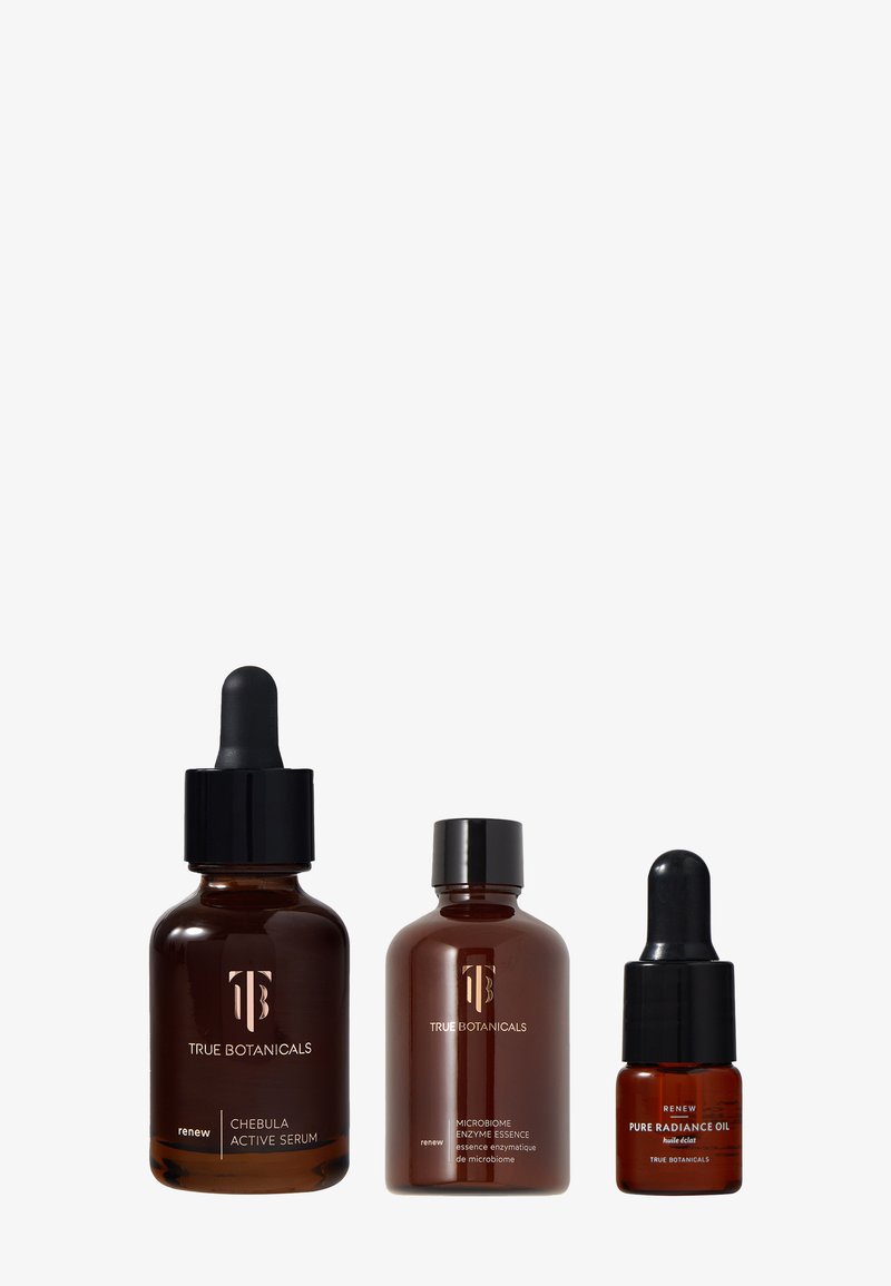 Trois bouteilles en verre ambré foncé avec des compte-gouttes et des bouchons noirs, étiquetées "Sérum Actif Chebula", "Essence Enzyme Microbiome" et "Huile Pure Radiance".