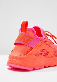 Nike boty s živě neonově oranžovým síťovaným svrškem, růžovými akcenty, polstrovanou podrážkou a výrazným páskem s logem přes střed nohy.