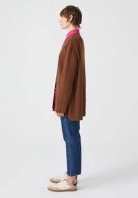 Barna kordbársony oversized kardigán egy rózsaszín galléros ing fölött, kék egyenes szárú farmernadrággal és fehér-barna sportcipőkkel párosítva.