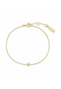 Guldarmband med en enda rund klar ädelsten i mitten, med en liten varumärkesetikett fäst nära låset.