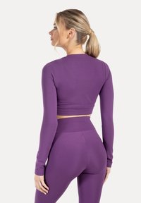 Fioletowy, długi rękaw crop top w połączeniu z legginsami z wysokim stanem. Gładki, elastyczny materiał zapewnia dopasowaną sylwetkę. Brak widocznych elementów ozdobnych i wzorów.