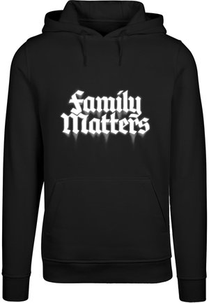 Svart hoodies med en frontficka och vit gotisk stil text "Familjens Betydelse" över bröstet, med en strukturerad yta.
