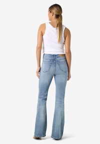 Φαρδιά τζιν παντελόνια σε ανοιχτό μπλε χρώμα, από τζιν ύφασμα με ελαφρύ ξεθώριασμα, μεσαίο ύψος μέσης και δύο τσέπες στο πίσω μέρος, συνδυασμένα με λευκό αμάνικο τοπ.