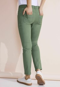 Vihreät puuvillahousut, joissa on kapea malli ja nilkkapituisuus, taka taskut ja sileä rakenne, yhdistetty valkoisiin tennareihin.