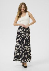 Gonna maxi in nero e beige, con un motivo astratto, vita arricciata e strati sovrapposti. Abbinata a una canotta bianca e a ballerine nere.
