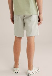 Helle graue Shorts aus Baumwolle mit zwei Gesäßtaschen und einer subtilen Textur. Getragen mit weißen Sneakers und einem grünen Shirt.