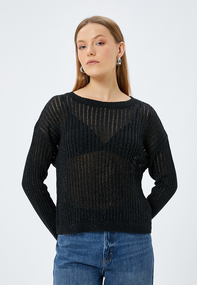 Svart stickad tröja med ribbad struktur, har en lös passform, vid nacköppning och något genomskinlig design. Tillsammans med blå jeans.