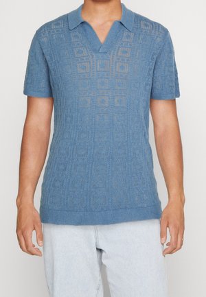 Polo en maille bleu clair avec un motif texturé, manches courtes et col en V. Il présente un ourlet côtelé et un col contrastant.