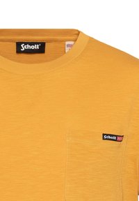 Kurzärmeliges gelbes T-Shirt aus strukturiertem Stoff mit Rundhalsausschnitt, ausgestattet mit einer Brusttasche und einem schwarzen "Schott N.Y.C."-Logo.