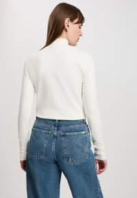 Biała bluzka z długim rękawem typu golf, dopasowana w okolicy szyi, w połączeniu z dżinsami w kolorze niebieskim o wysokim stanie, z klasycznym czteropocketowym wzorem.