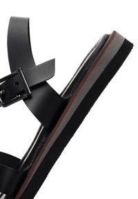 Black leather sandal with a wide strap and adjustable buckle. Features a thick sole in gray and brown layers. Smooth texture, modern design.