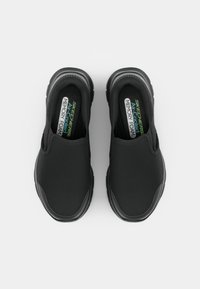 Black slip-on shoes with a textured mesh upper and cushioned memory foam insoles. Rounded toe and thick rubber sole.