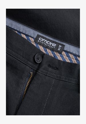 Mustat kangashousut, joissa on hienovarainen tekstuurikuvio. Varustettu vetskareilla, napituksella ja raidallisella vuorilla. Brändilogo näkyvissä.