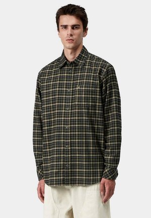 Camisa de cuadros verde y negro con cuello, mangas largas, bolsillo frontal y una textura suave. Botones metálicos visibles en la parte delantera.