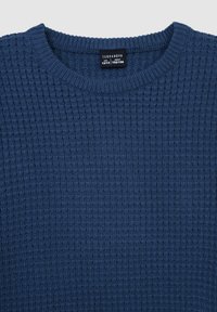 Granatowy sweter wykonany z fakturowanej dzianiny. Posiada okrągły dekolt i ściągacze na mankietach. Widać metkę z rozmiarem i marką "Terranova."