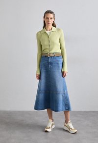 Light green ribbed long-sleeve top, buttoned front. Denim A-line skirt with horizontal seam. White sneakers with gold accents.
