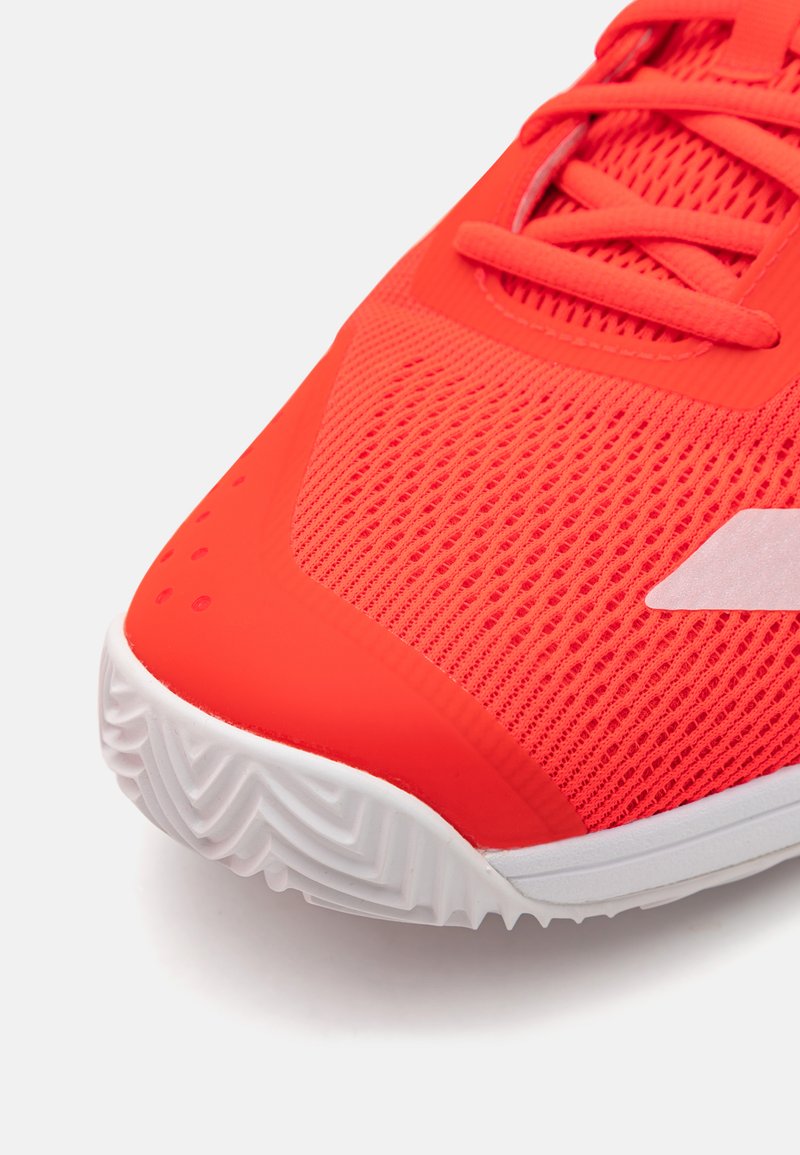 Leuchtend roter Sportschuh mit einem strukturierten Mesh-Obermaterial, verstärkter Zehenpartie und einer weißen Gummisohle mit einem Zickzackmuster.