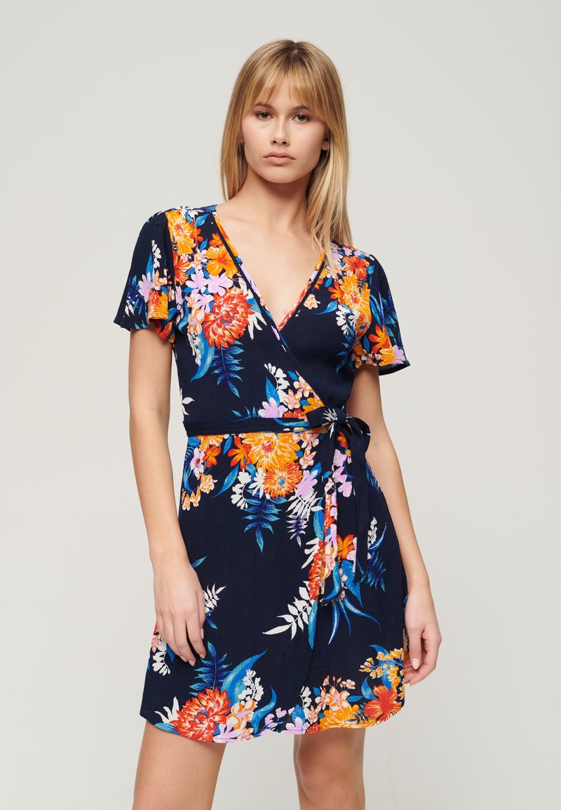 Abito a portafoglio floreale in blu navy con fiori arancioni, rosa e bianchi. Maniche corte, scollatura a V e dettaglio con cintura in vita. Tessuto morbido.