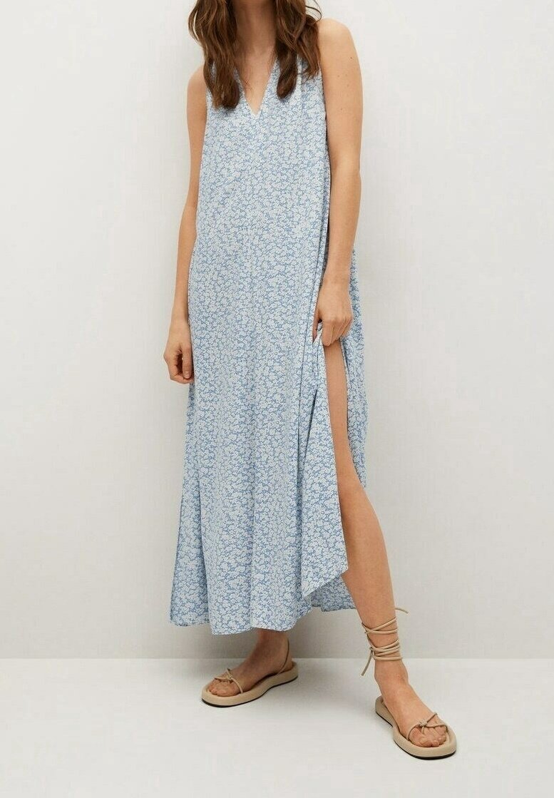 Robe maxi longue bleue claire à motif floral avec décolleté en V, fente latérale et tissu fluide. Portée avec des sandales plates beiges avec des lanières autour de la cheville.