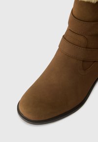 Brune ruskinds ankelstøvle med en glat tekstur, rund tå og to justerbare remme. Sort gummisål i bunden.