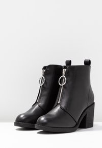 Bottines en cuir noir à bout pointu, avec fermetures éclair argentées à l'avant et talon carré texturé. Dotées d'anneaux pour un enfilage facile.