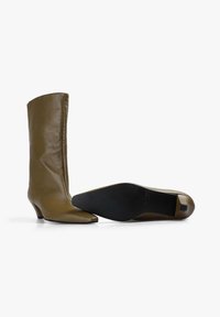 Botas de cuero marrón hasta la pantorrilla con un bajo tacón kitten, una bota en posición vertical y la otra acostada de lado mostrando una suela negra.